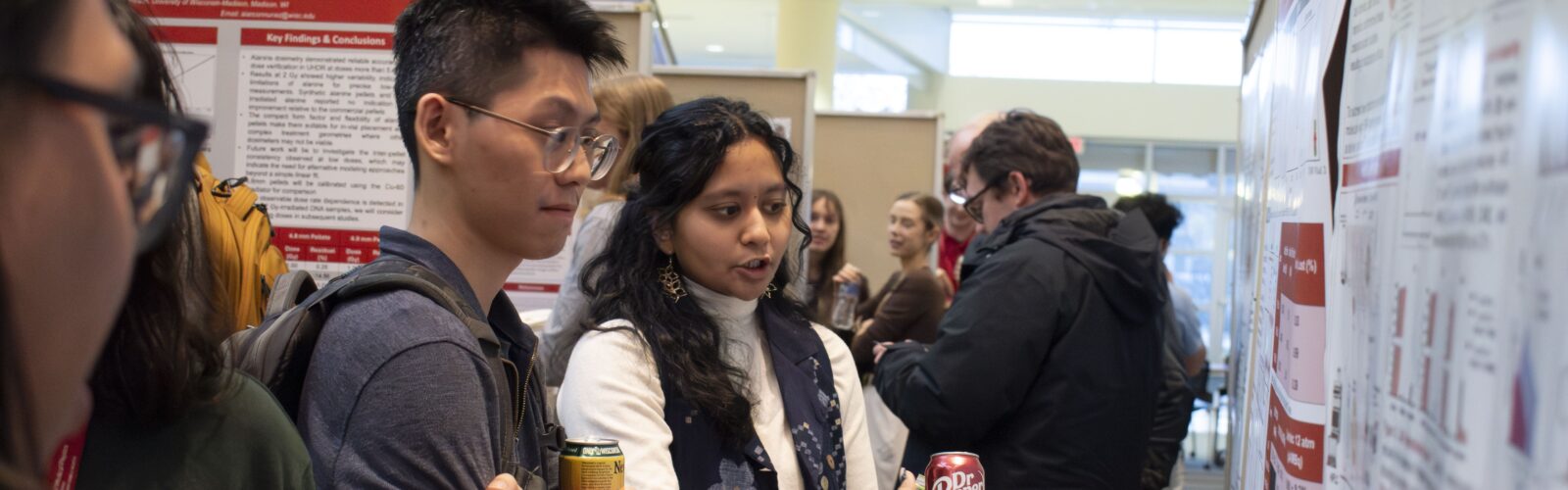 two students stand together and discuss a poster in front of them