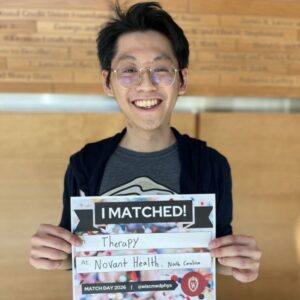 Alex Kuo stands in the WIMR lobby holding a I Matched sign