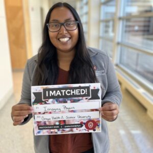Lucky stands in a long hallway and holds an I matched sign