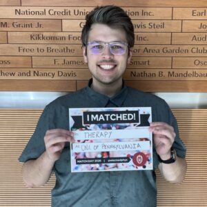 Nicholas stands in the WIMR lobby holding a sign that says I matched