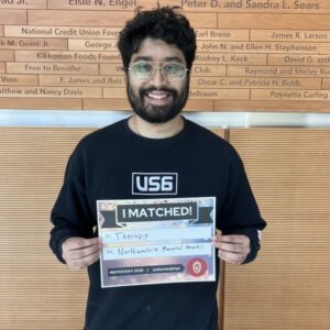 Tarun stands in the lobby at WIMR holding an I matched sign
