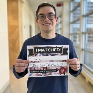 Will stands in a long hallway holding a sign that says I matched