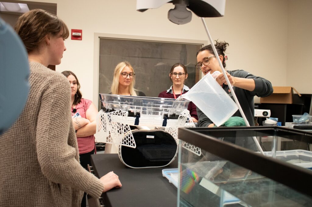 Group of people stand over an exam table while a person on the right pours water into a wide bowl