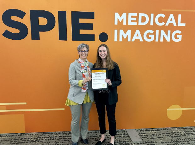 two people stand holding a certificate in front of a large orange banner that says SPIE Medical Imaging