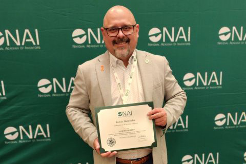 Reinier stands in front of a green background that says NAI repeatedly and holding an award certificate