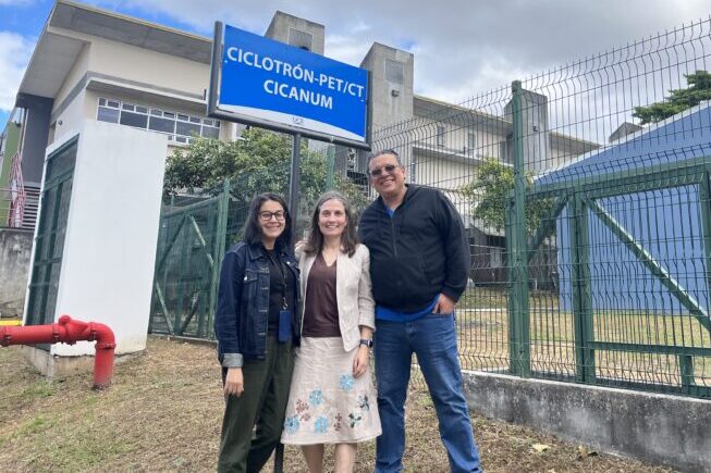 three people stand in front of a building with a green fence on their right in Costa Rica